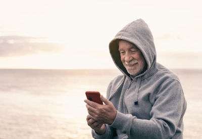 Smiling senior man using mobile phone while standing against sea