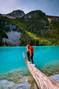 Rear view of men standing by lake against mountains