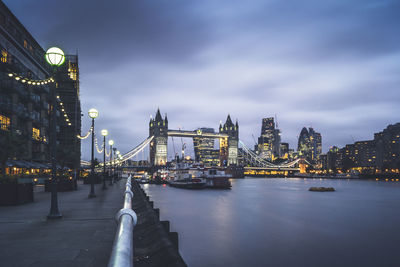 Illuminated city at waterfront against cloudy sky