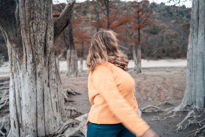 Rear view of woman standing by tree trunk in forest