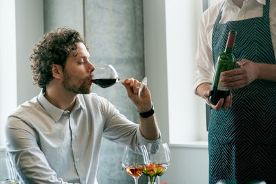 Midsection of bartender standing by customer drinking wine in tasting room