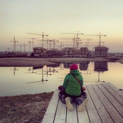 Rear view of woman sitting on pier against sky