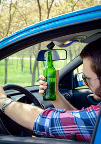 Man holding beer bottle while driving car in forest