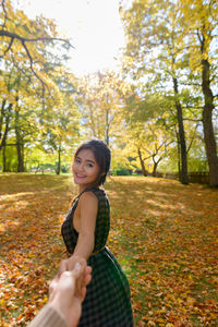 Portrait of smiling young woman standing by tree during autumn