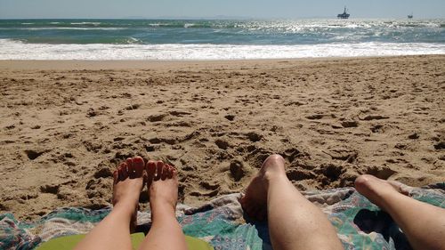 Low section of friends relaxing at sandy beach