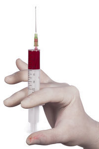 Close-up of hand holding syringe with blood over white background