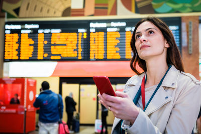 Young businesswoman holding smart phone while looking up