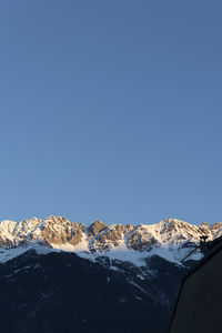 Low angle view of snowcapped mountains against clear blue sky