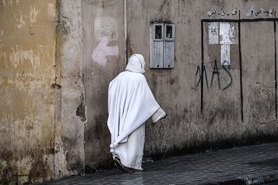 Rear view of moroccan woman in traditional clothing walking along historic wall