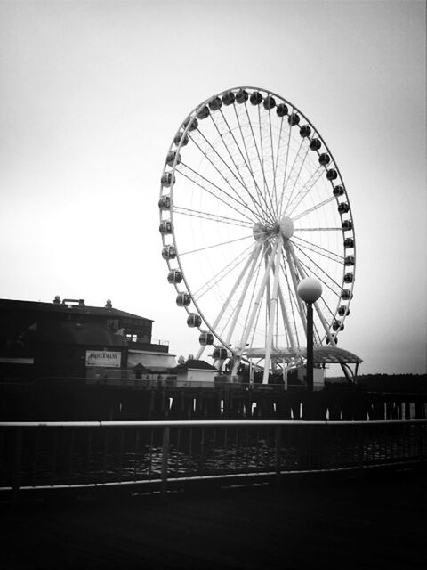 ferris wheel, amusement park ride, amusement park, arts culture and entertainment, built structure, low angle view, architecture, sky, circle, clear sky, copy space, building exterior, wheel, outdoors, no people, day, transportation, geometric shape, metal, incidental people