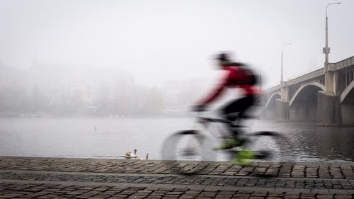 Side view of a blurred man bicycling against river