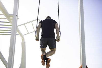 Low angle view of man exercising on gymnastic rings against sky
