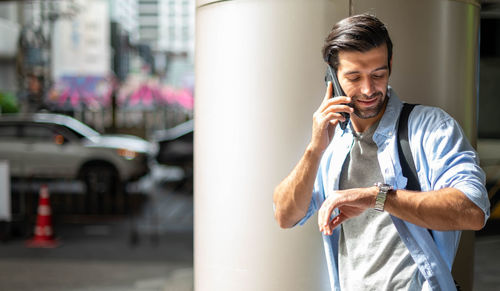 A young caucasian man watching the time and calling on his cell phone while waiting for his friend.