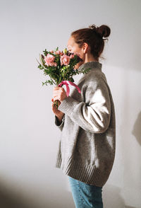 Woman in grey knitted sweater with bouqet of flowers in hands on white background