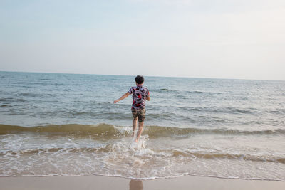 Rear view of man running at beach against sky