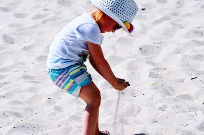 Side view of girl playing with sand at beach during summer