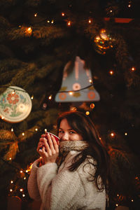 Happy teenage girl holding mulled wine standing by christmas tree christmas tree