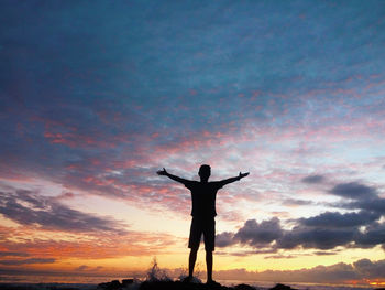 Silhouette man with arms outstretched standing against sky during sunset