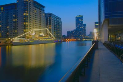 Illuminated bridge over river by buildings in city at night