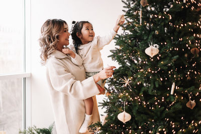 Asian multiracial mom and little daughter celebrate christmas holiday in decorated house