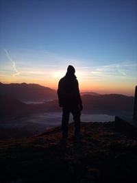 Rear view of man standing on mountain against sky during sunset