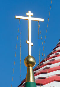 Low angle view of cross amidst buildings against clear blue sky