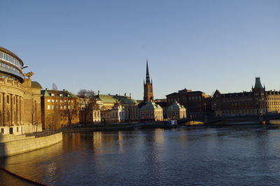 Buildings by river against clear sky in city