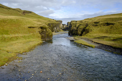 Stream flowing amidst land against sky