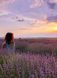 Woman looking away while standing amidst lavender flowers during sunset