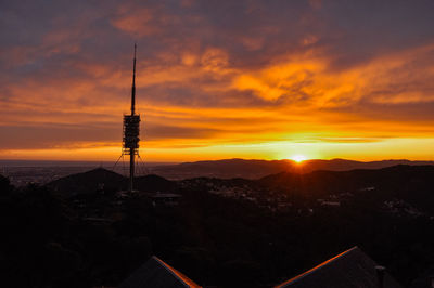 Silhouette communications tower and buildings against orange sky