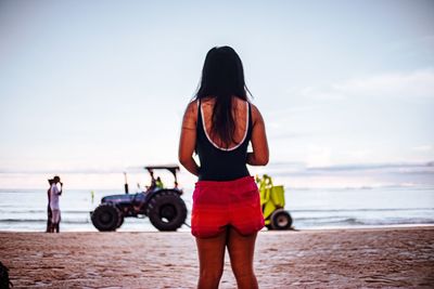 Rear view of women standing at beach against sky