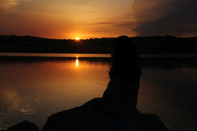 Silhouette woman by lake against sky during sunset