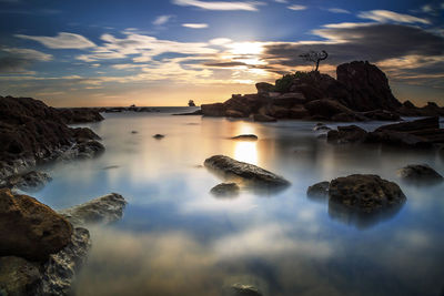 Rocks in sea against sky during sunset