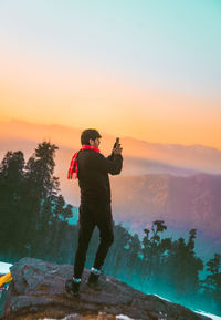 Rear view of man standing on mountain against sky during sunset