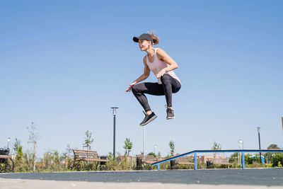 Woman in sportclothes working out on the sports ground in sunny summer day, jumping knees to hands
