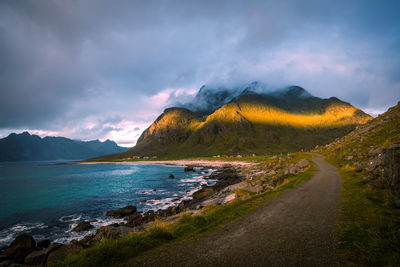 Scenic view of sea, dirt road and mountains against sky during sunset, lofoten, norway