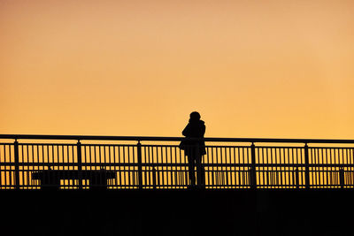 Silhouette man standing by railing against sky during sunset