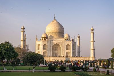 People visiting taj mahal against blue sky during sunset