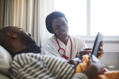 Smiling healthcare worker showing digital tablet to patient during routine checkup in hospital ward