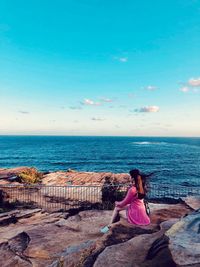 Woman sitting on rock by sea against sky