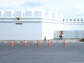 Side view of person with umbrella walking on footpath against white wall