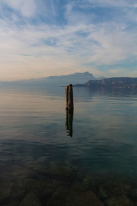 Wooden post in sea against sky during sunset