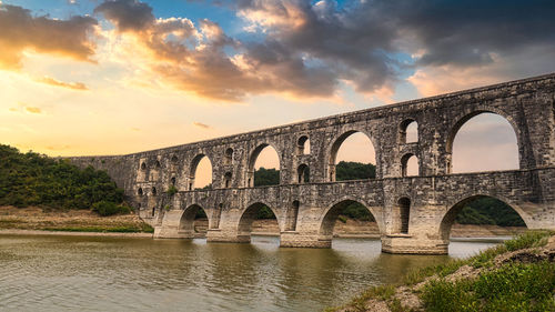 Arch bridge over river against sky during sunset