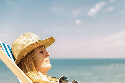 Portrait of young woman with hat on beach against sky