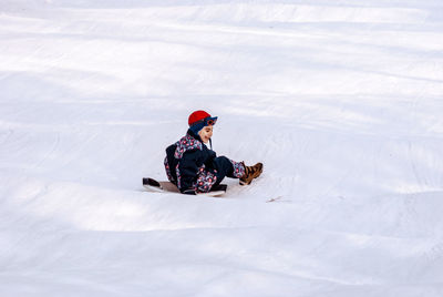 Smiling boy tobogganing on snow covered field during winter