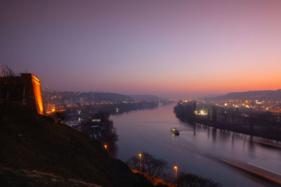 High angle view of illuminated buildings by river against sky at sunset