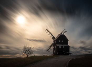 Traditional windmill by road against sky during sunset