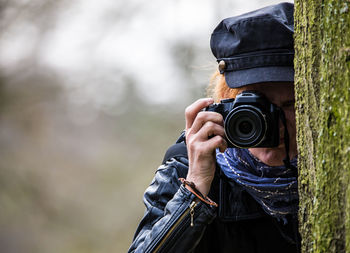 Woman photographing through camera by tree