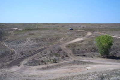 Dirt road on field against clear sky