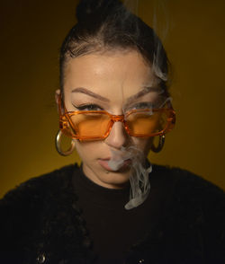Portrait of woman wearing sunglasses smoking against brown background